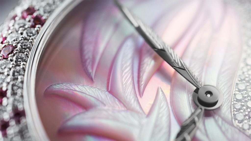 La esfera de esta excelsa creación luce nácar natural sobre oro blanco En la mitad superior –la que vemos aquí– luce decoración de plumas grabada a mano En la mitad inferior llevaba un engaste “efecto nieve” con piedras preciosas de diversos diámetros (diamantes y zafiros rosas. Las agujas de horas y minutos tipo “hoja” de oro blanco están grabadas a mano.